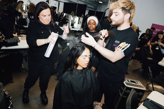 Hair stylists finishing a runway hairstyle backstage with professional styling products at London Fashion Week with Sally Beauty.