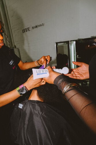 Stylist applying UNITE Smooth & Shine styling cream backstage during London Fashion Week with Sally Beauty.